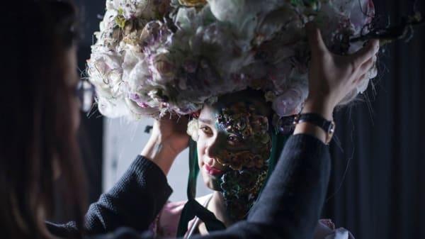 A model having a large floral headpiece adjusted on her head