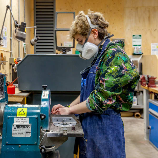 Girl in mask operating machinery in a workshop 