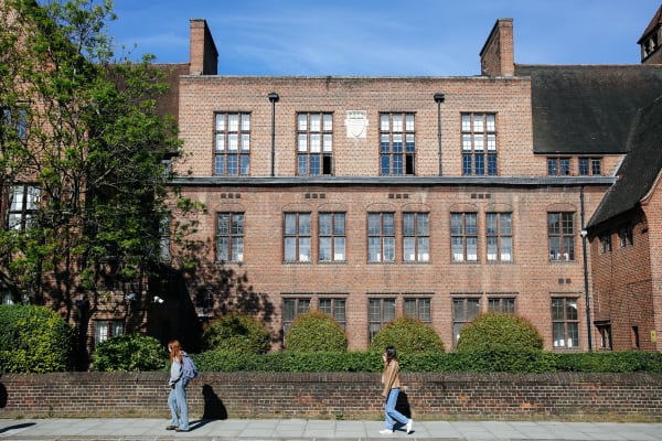 Two people walking on the street in front of an grand, old brick building.