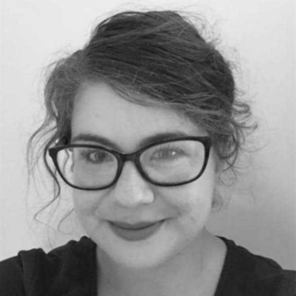 Claire Bunyan, Senior Research Fellow in Cultural Anthropology, is smiling at the camera and wearing a pair of thick framed glasses
