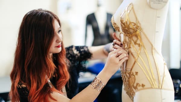 A student adjusting stitching on an item on mannequin 
