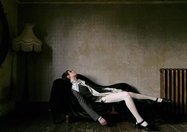 Male model in dress clothes lounging on a sofa in an upper-class styled living room.