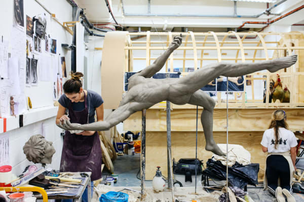 Girl working on a male figure in clay 