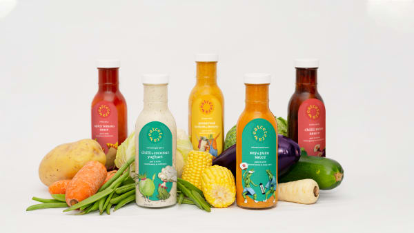 An array of food products including bottles, sitting amongst vegetables.