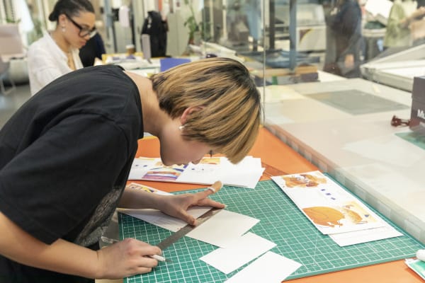 A student in a workshop, measuring paper to cut.