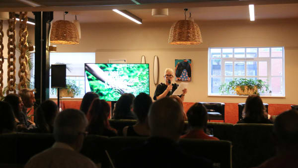 Lady talking in front of a seated crowd.