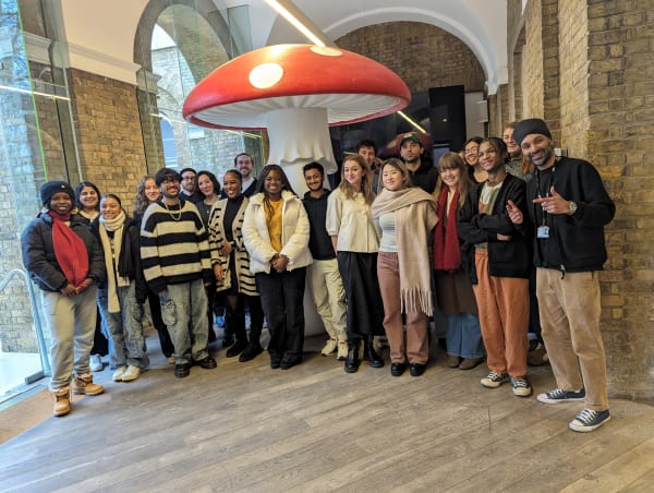 Photograph of a group of students standing infront of a sculpture of a giant red and white mushroom