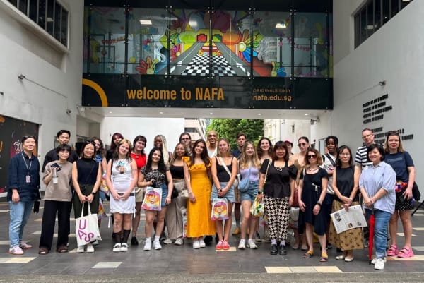 Image shows a group of around 25 people standing in front of a building that reads ‘Welcome to NAFA’ 
