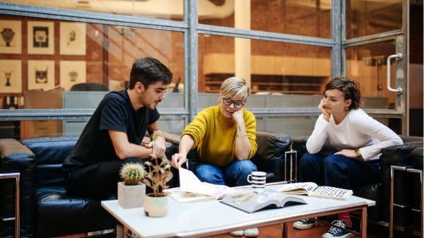 Two students sit in an office and look through work. 