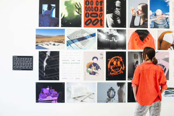 Girl in orange jacket standing in front of a wall of prints 