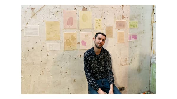 Tim sits in front of a wall with prints of leaves behind them