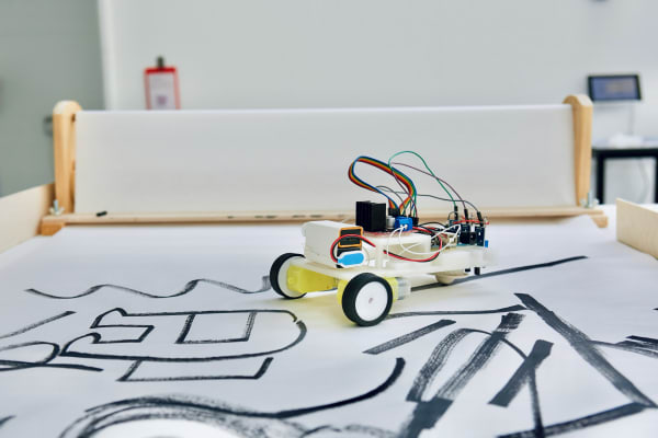 Photo of a small battery powered robot following black lines on a large roll of paper