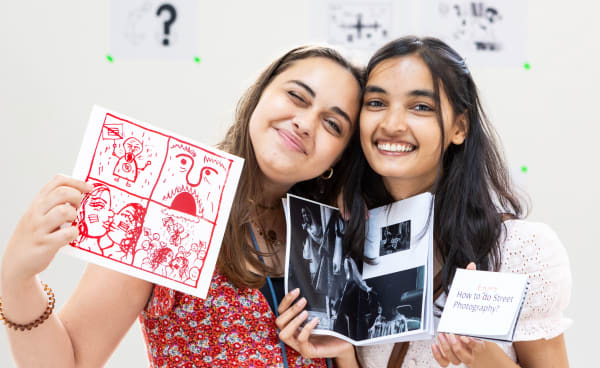 2 students holding up work and smiling