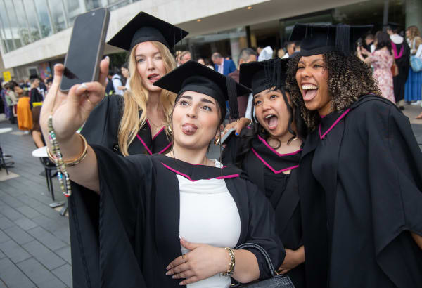 A group of graduates taking a photo at the Royal Festival Hall and pointing towards the camera