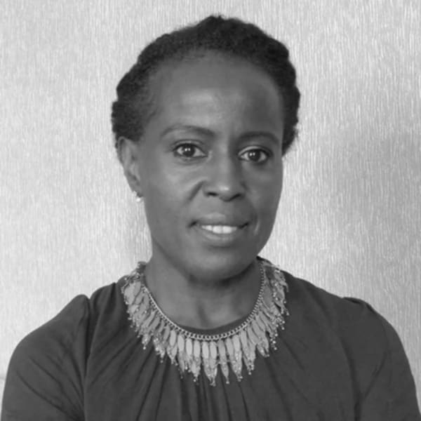 Michelle is standing in front of a grey background, wearing a black top and a large necklace with leave-shaped beads