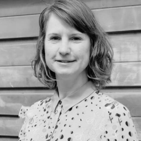 Jana Riedel, XR Project Manager, standing in front of a wall wearing a floral blouse and smiling at the camera. The photo is in black and white. 