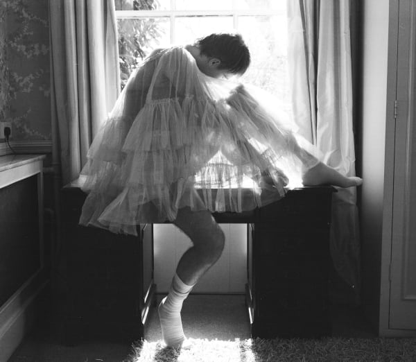 Black and white photograph of a dancer, folded, by a window.