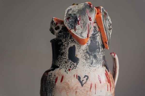 Close-up of an artistic ceramic pitcher adorned with abstract black and red designs. Features textured elements and a hand-drawn heart, creating a raw, expressive feel.