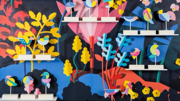 Miniature bird statues in front of a very colourful painted background of plants and trees