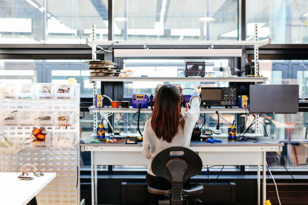 Image from behind a women sat at a desk surrounded by lots of tech equipment, UAL Creative Computing Institute, MSc Creative Computing, Anna Tsuda in the studio, Copyright holder: Alys Tomlinson