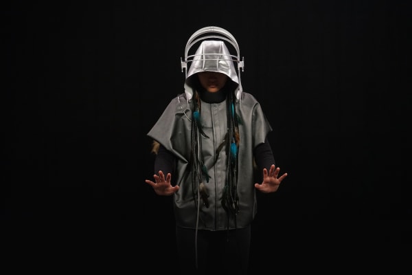 Photo of a person wearing a grey jacket and silver hood with large headphones over the top