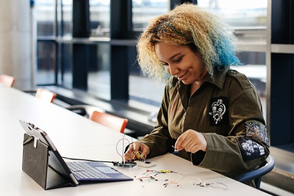 Woman sitting at desk holding wires next to open laptop