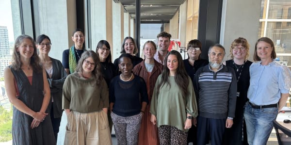 Group photo of appoximately 20 people standing in an office with large windows 