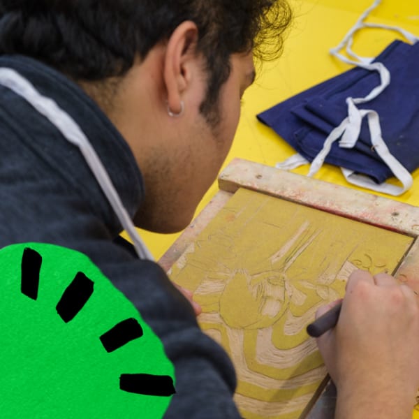 A student working on a lino or wood cut. The background and material they're cutting from are shades of yellow. 
