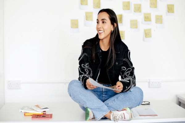 Lady sat cross legged on white tabletop looking to the left in classroom setting