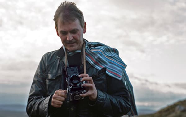 A picture of a man standing outside holding a vintage camera.