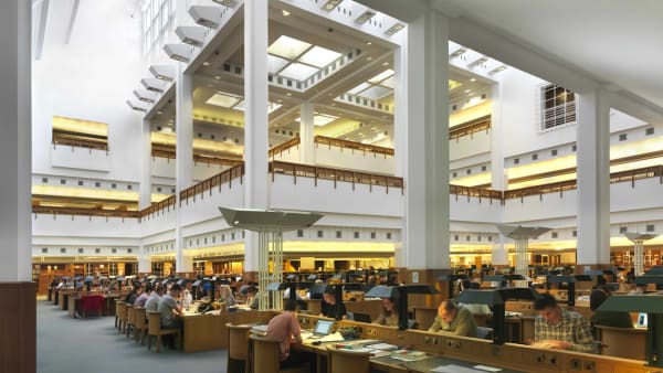 People working at traditional looking desks inside a large airy room