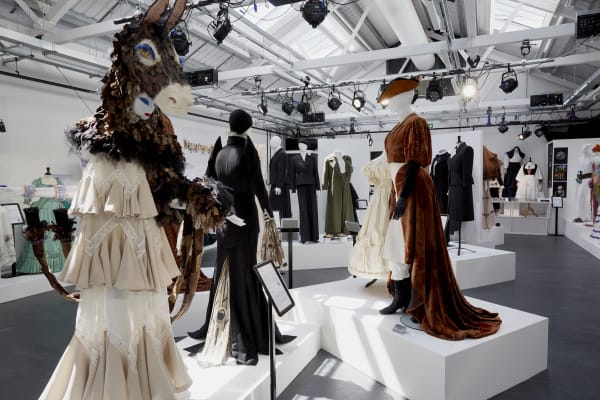 A room shot of lots of mannequins dressed in costumes of different colours and materials. One mannequin has a model donkey head