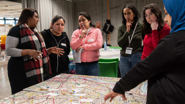 Several people from different backgrounds and ethnicities are around a table. On the table, there is a map.