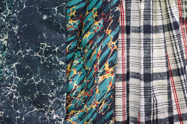 A close-up of three fabric patterns: dark blue with white marbling, vibrant green and red with yellow swirls, and black and red plaid on white.
