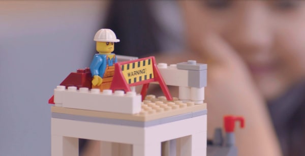 Close up still from a film. Lego tower with a lego construction worker.