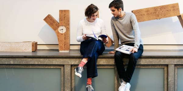 Two students sitting on a ledge near a clock