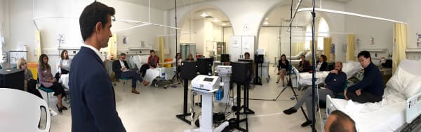 hospital room full with people listening to a person introducing a piece of technology.