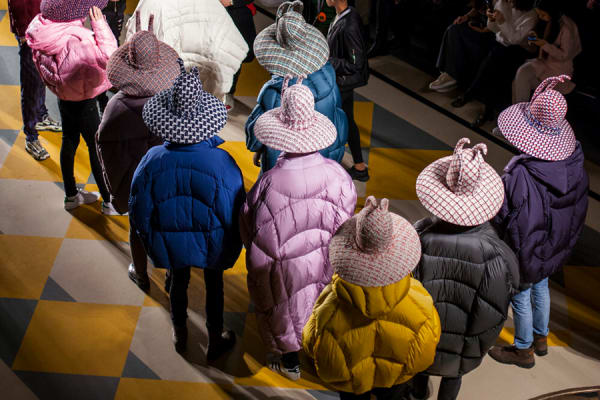 Birds-eye view of a catwalk featuring people wearing colourful textured hats and puffer coats.