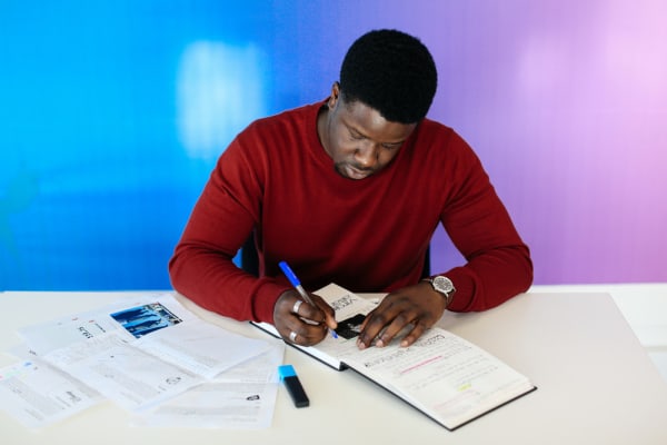 Man writing in a notepad with a colourful blue and purple screen behind him