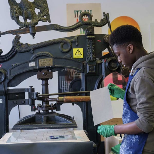 A student standing at a traditional ornate printing press 
