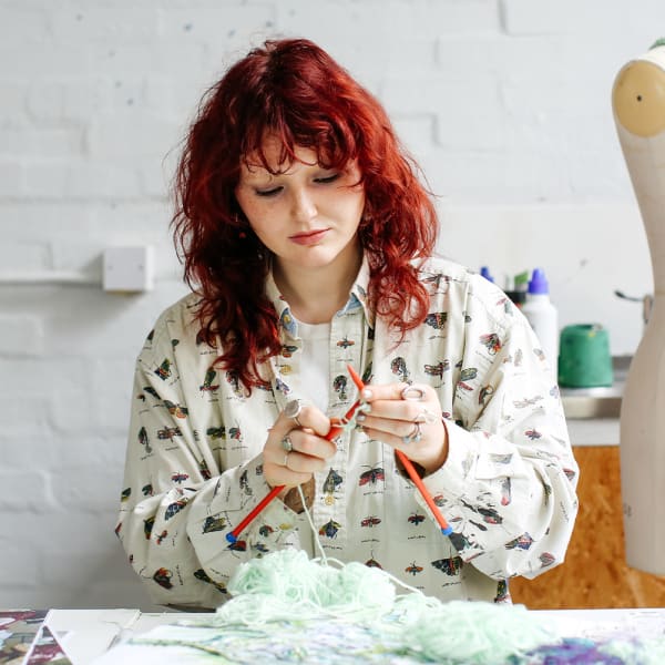 A student knits stitches with mint green wool.