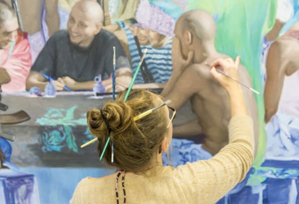 Student standing painting with paintbrushes pinned up in their hair