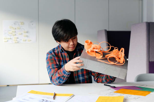 Student at a desk holding an orange sculpture