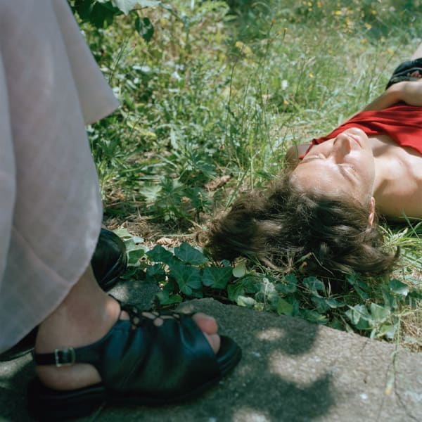 Photograph of a woman lying on the grass next to a pair of feet