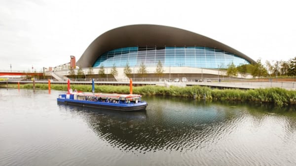View of a river with a boat, with a backdrop of a big arching building.