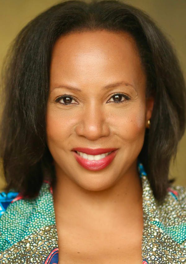 Suzann McLean MBE smiling close to the camera against a tan backdrop.