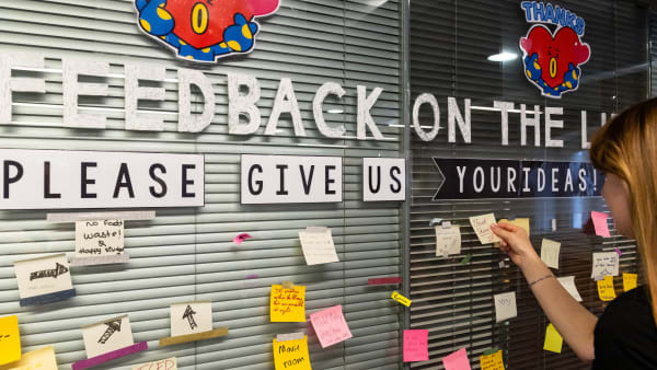 Student placing post it note on glass wall containing more post it notes with feedback suggestions