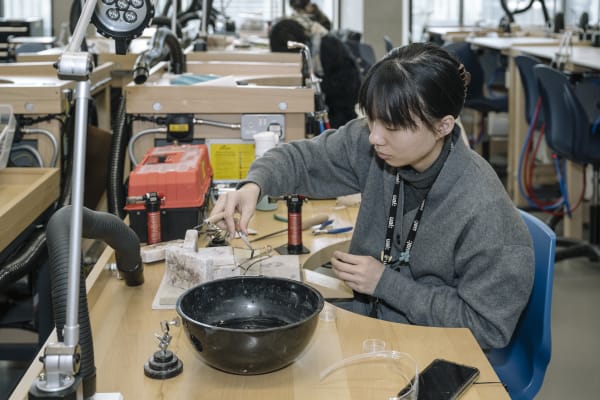A student is sitting at a desk crafting a piece of metal jewellery.
