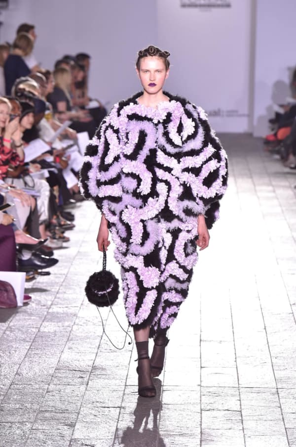 A model walking down a catwalk wearing a purple and black detailed garment