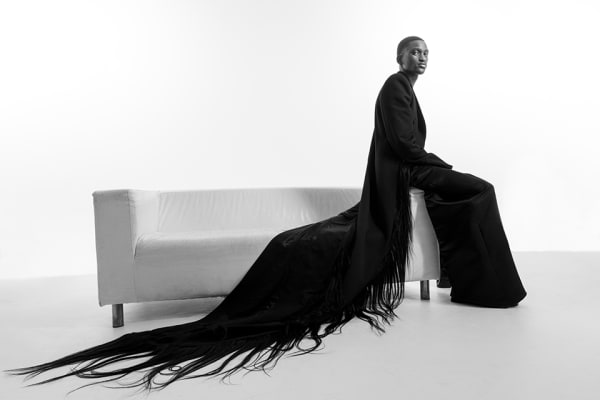 Seated black male model in black coat that trails into human hair.